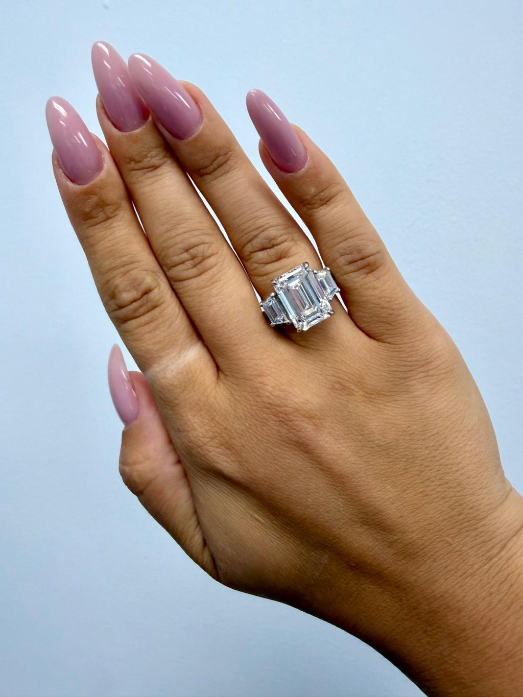 Vela emerald cut and trapezoid three-stone engagement ring worn on the hand