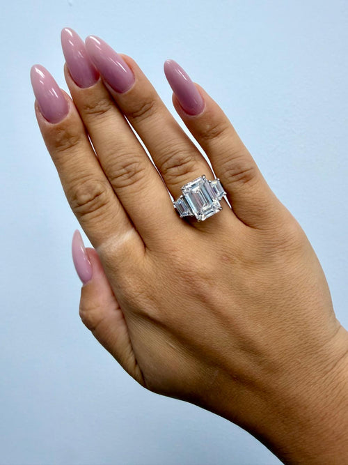 Vela emerald cut and trapezoid three-stone engagement ring worn on the hand